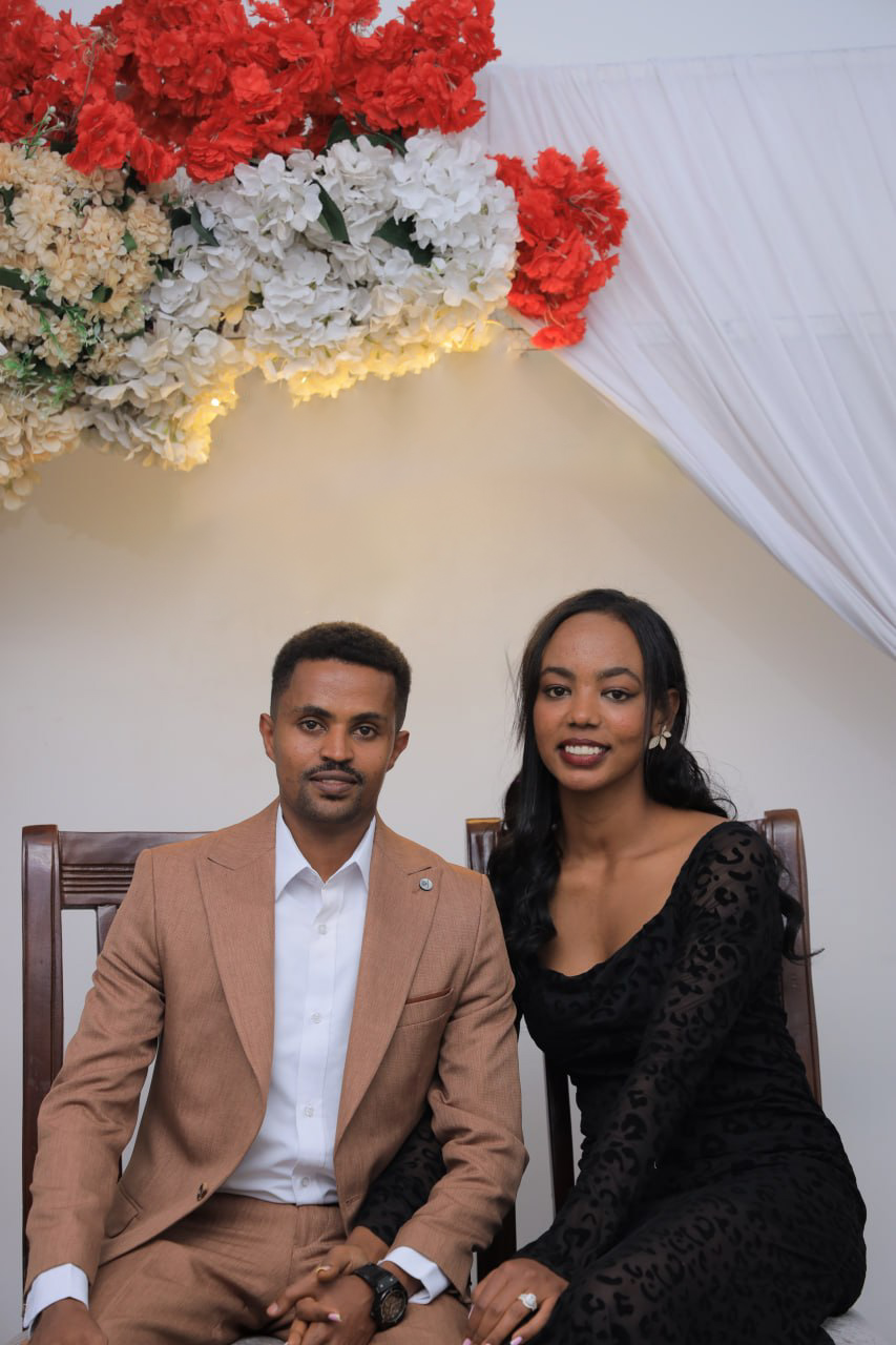The couple sitting together beneath wedding flowers